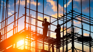 Silhouetted construction workers on scaffolding at sunset